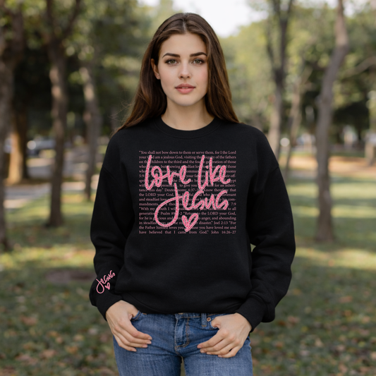 Model wearing Black Love Like Jesus sweatshirt with pink script lettering and heart design outdoors