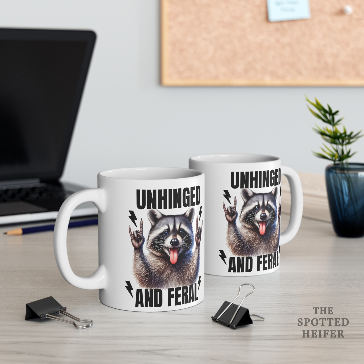 Two white Unhinged and Feral raccoon mugs on a desk with plants in the background, matching funny coffee mug set for friends.