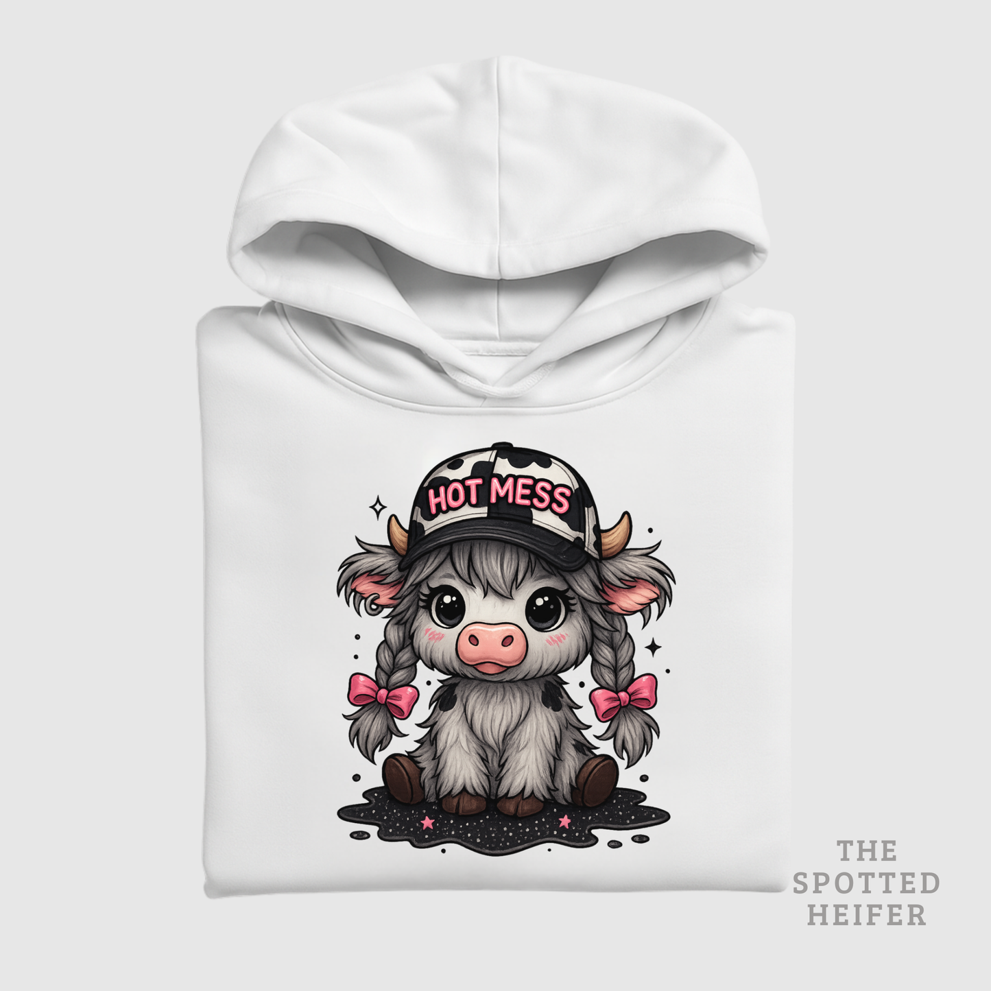 Folded white hoodie featuring Hot Mess cow design with pink bows, braids, and cow-print hat, The Spotted Heifer.