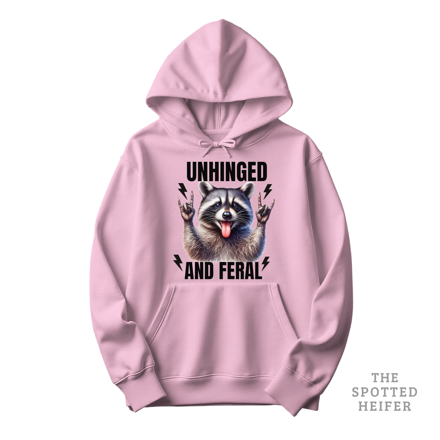 Light pink Gildan 18500 hoodie featuring “Unhinged and Feral” text with a cute raccoon graphic on the front – funny western hoodie by The Spotted Heifer.